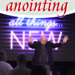 pastor with hands raising in front of sign that says all things new