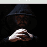 man sitting in dark hoodie in the dark looking creepy